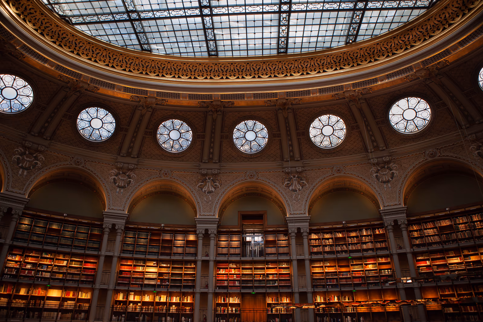 An ornate library with curved bookshelves beneath a glass dome
