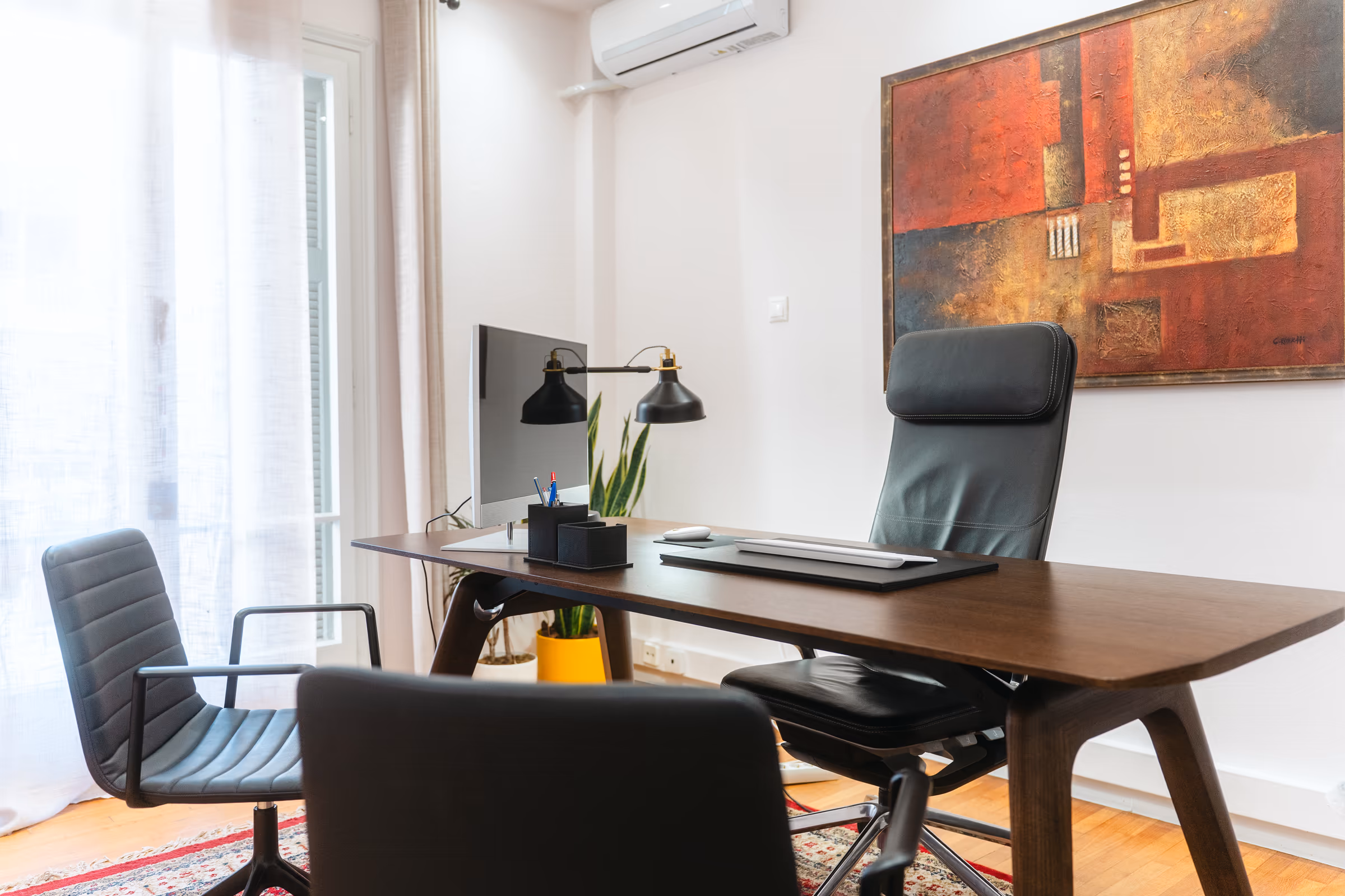 A walnut desk and leather chairs in a sunlit office, an abstract painting in red on the wall